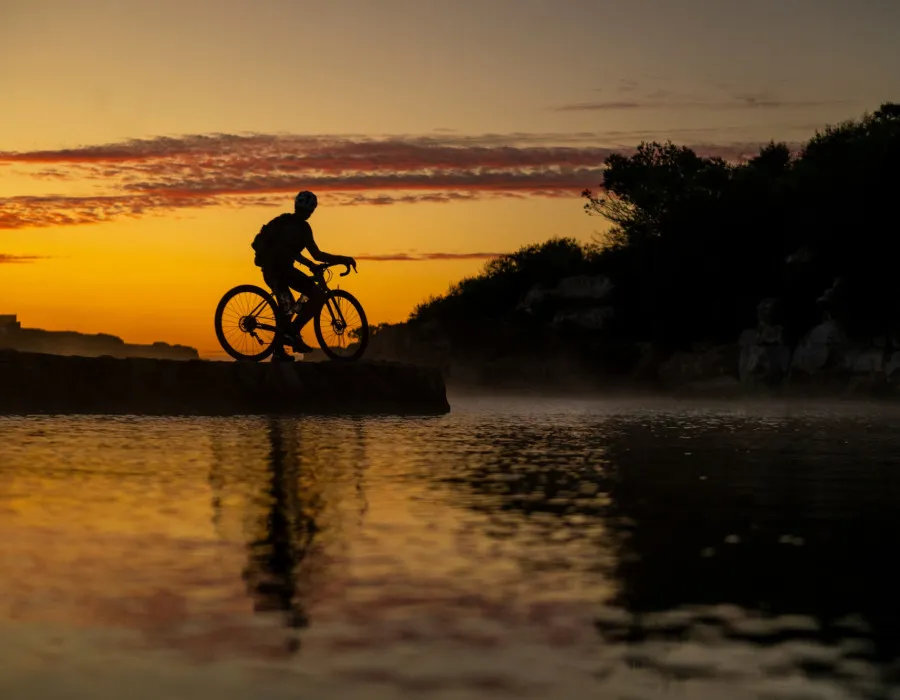 Silhouette of a lone cyclist, who has stopped by the water to admire the orange sky behind them