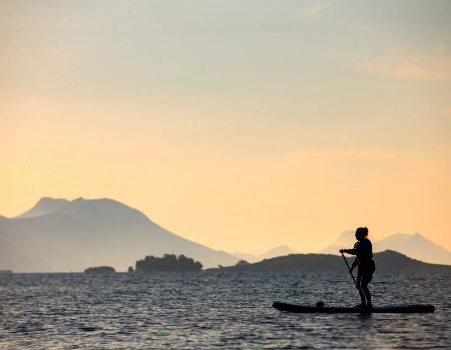 A lone event participant paddleboards across calm water, with a pink sky and hills in the background
