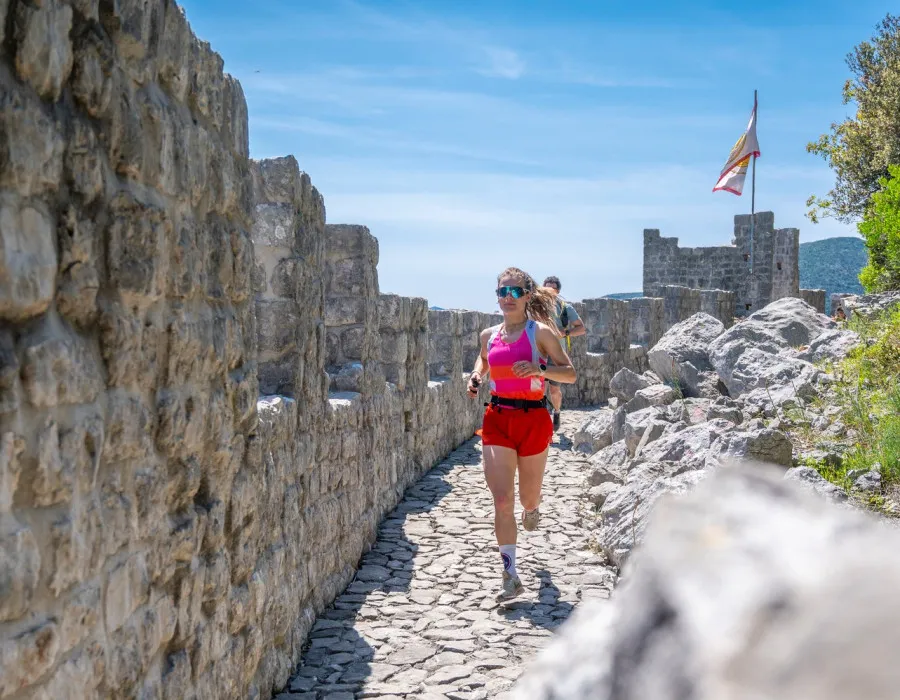 A man and a woman run next to a wall with a blue sunlit sky in the background