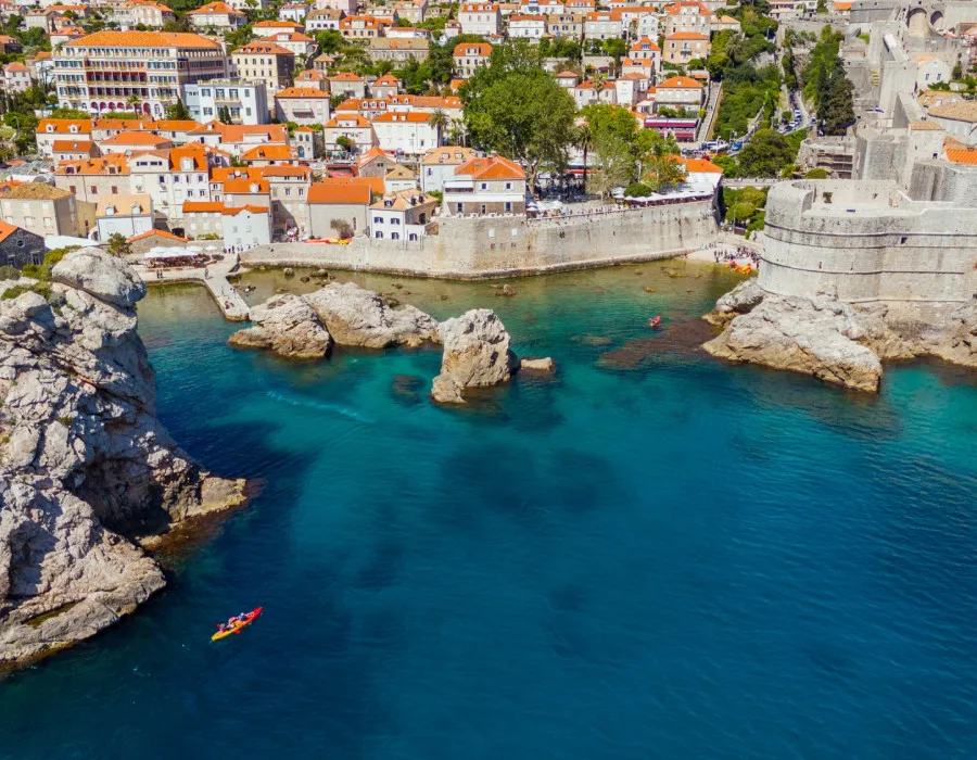 Kayaks glide across blue water, moving away from historic city walls and orange-roofed buildings