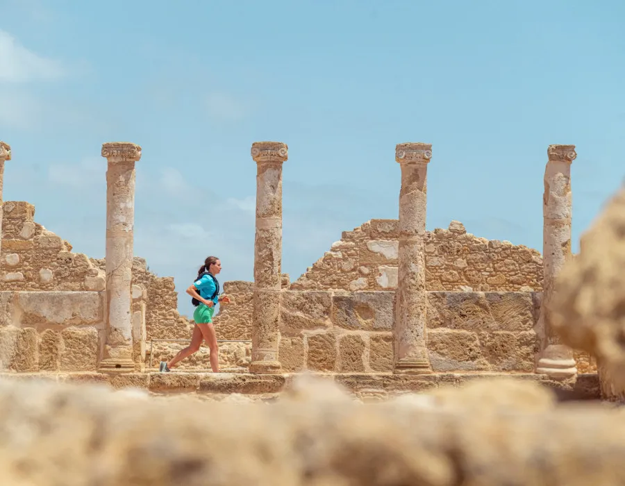 A participant runs through ancient stone ruins lined with tall columns beneath a bright blue sky