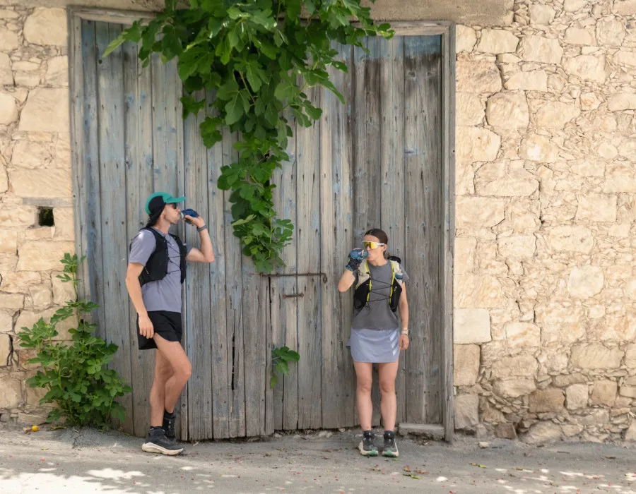 Man and woman stood by a big, wooden door and both having a drink from their water bottles