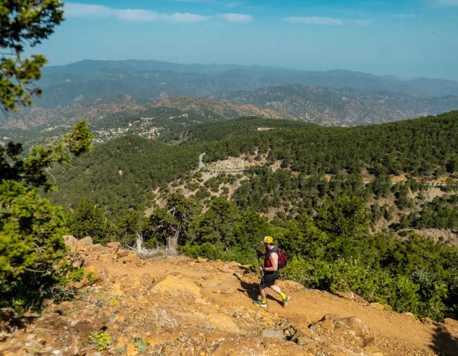 Man running along sandy and rocky terrain with greenery and mountains in the distance
