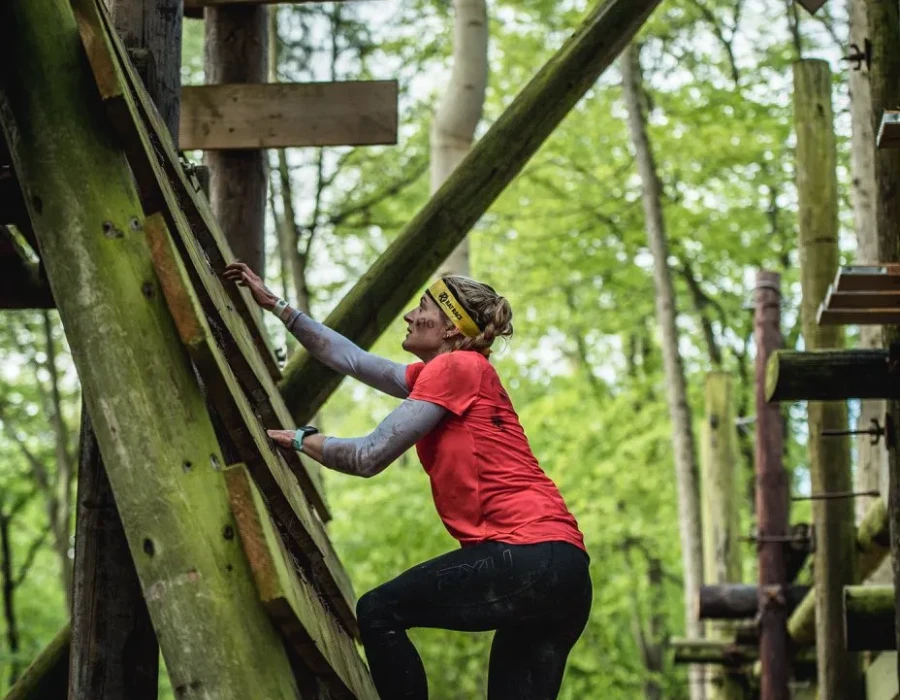 Woman climbing up a wooden ladder as part of an obstacle course in a forest