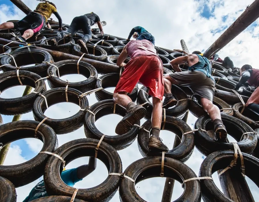 People climbing up a wall of tyres, under a cloudy sky
