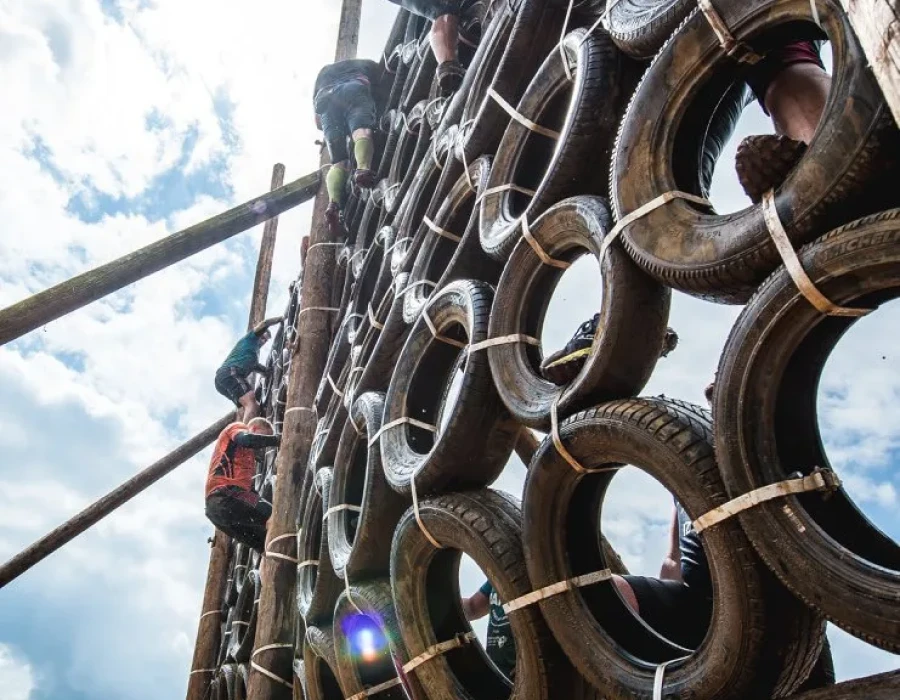 Participants climbing up a muddy wall of tyres