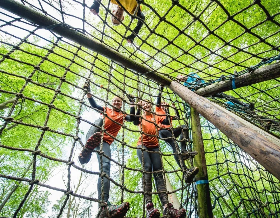 Smiling participants climbing up a rope obstacle in a forest