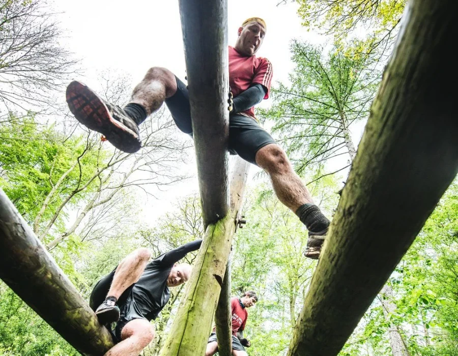 Men sliding across wooden poles as part of an obstacle course in a forest