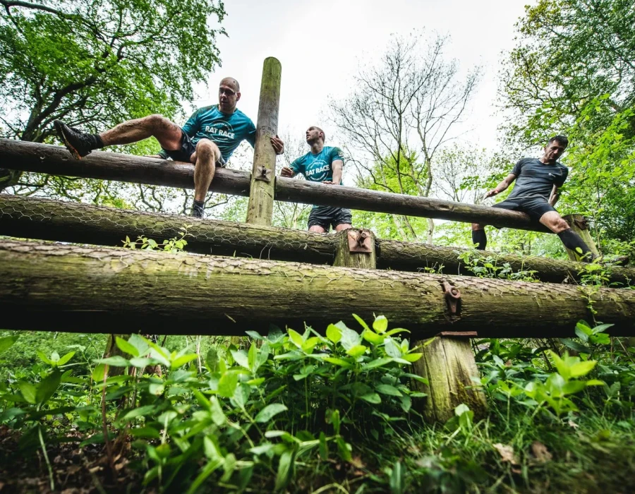 Men climbing over wooden poles as part of an obstacle course in a forest