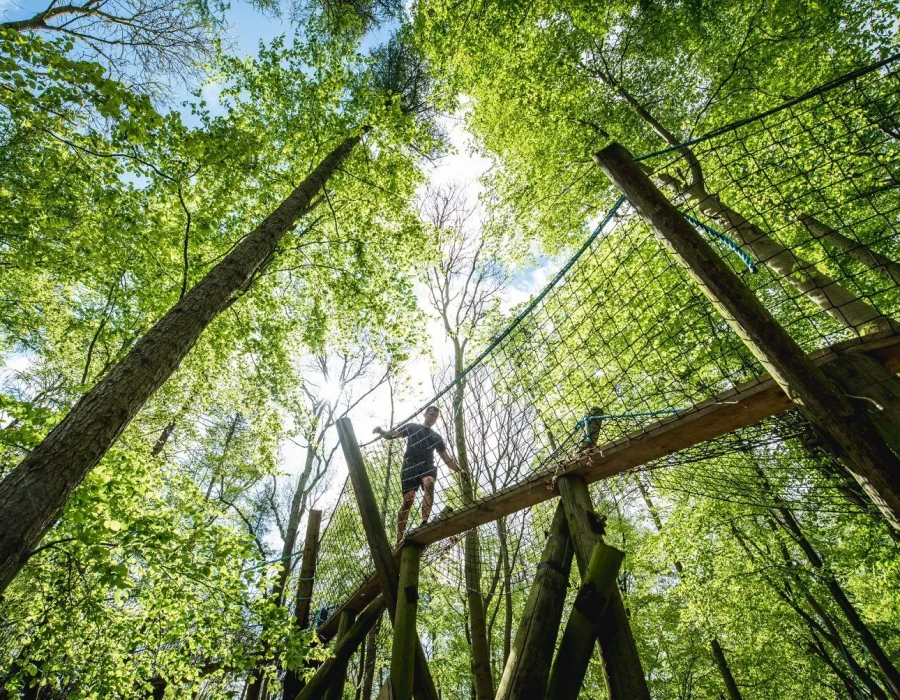 Man walking over a plank of wood, with netting either side