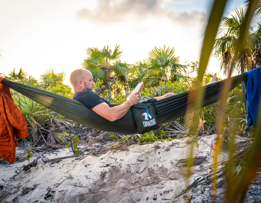 Man relaxing and reading a book in a hammock on a sandy beach