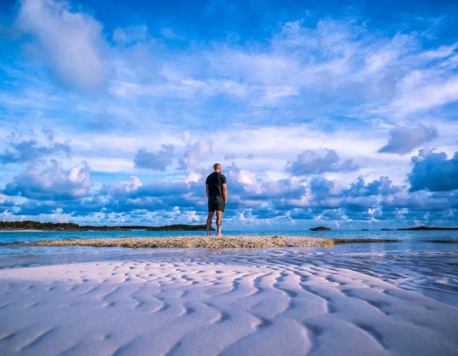 Man stood on a sandy beach looking out to the sea