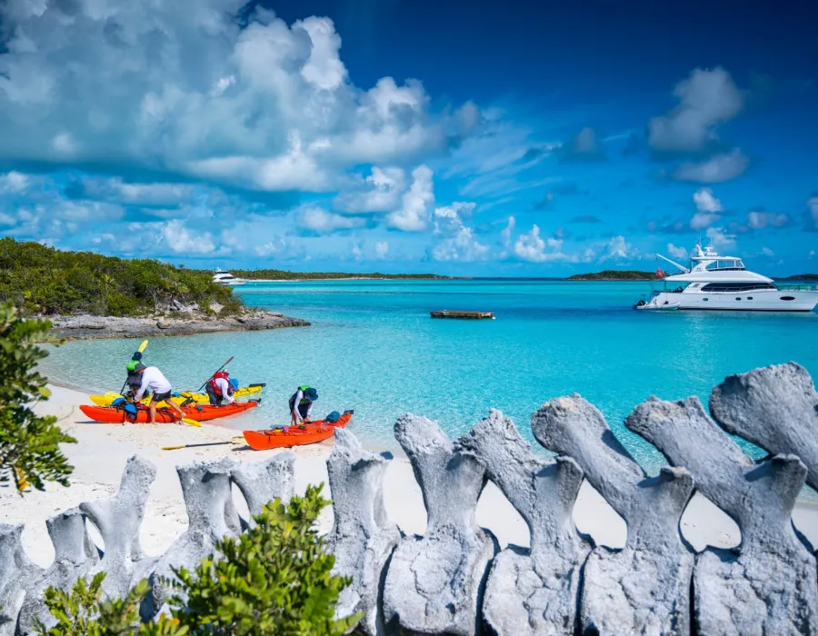 Participants and kayaks on the shoreline of a white sand beach