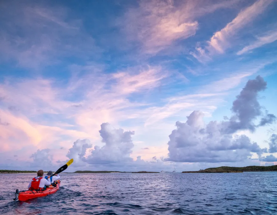 Two participants kayaking through water with colourful sky above