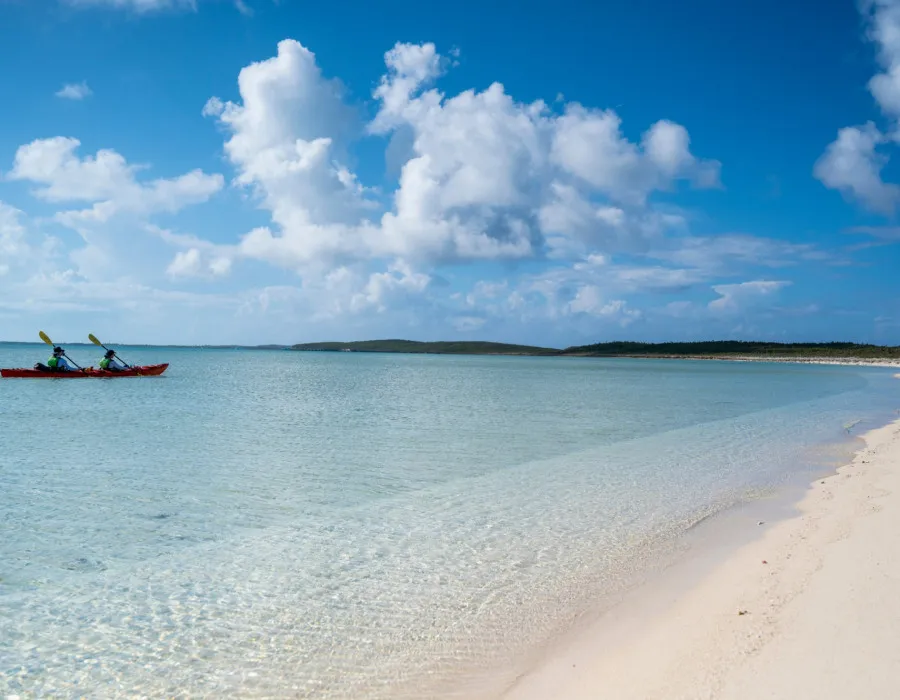 Two participants kayaking through shallow water near a sandy beach