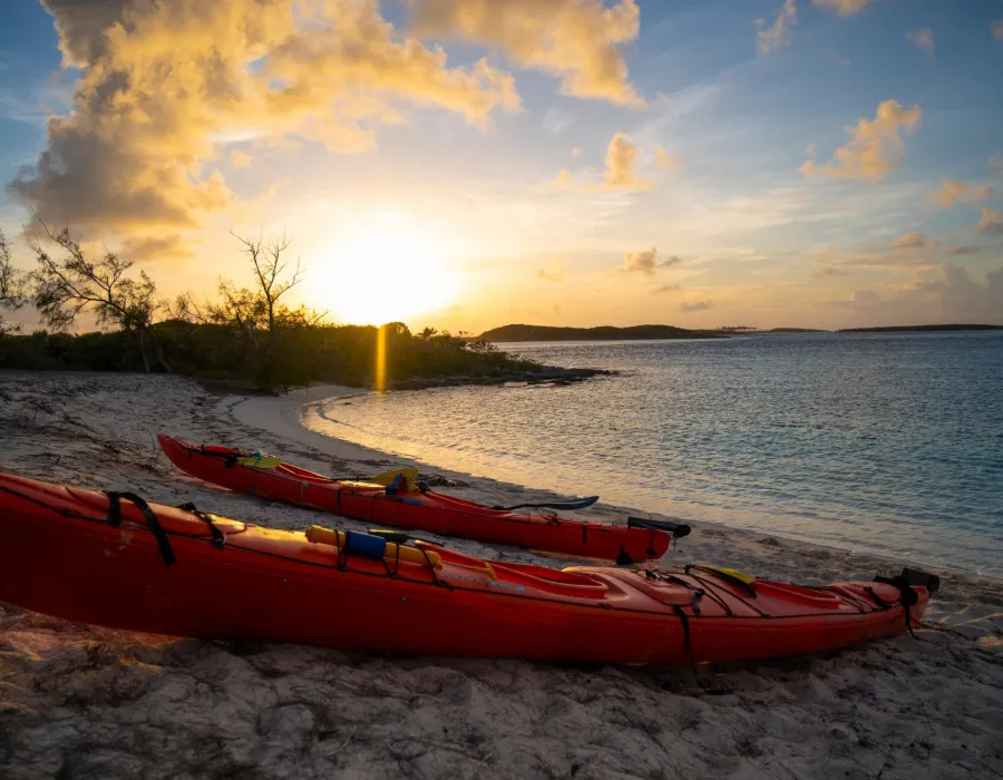 Two colourful kayaks on a sandy beach at sunset