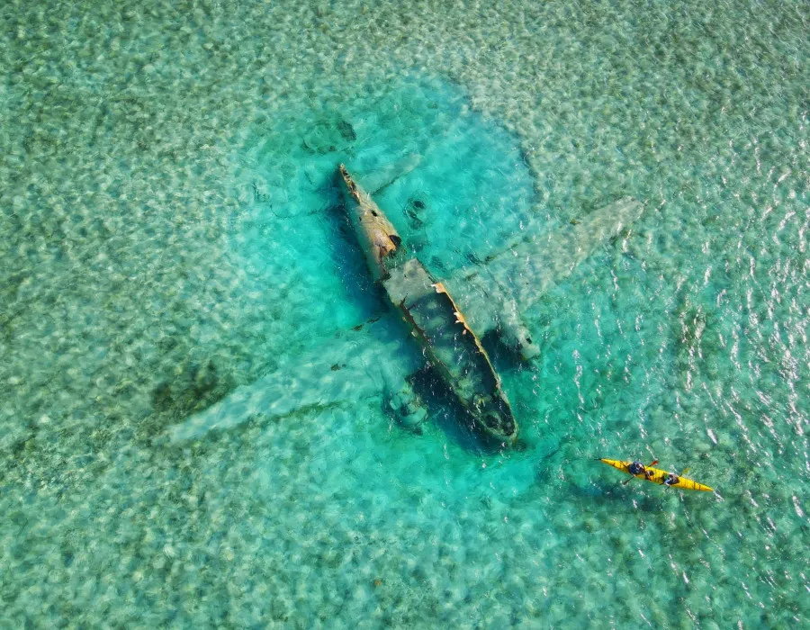 Participants kayaking through clear water with plane wreck below them
