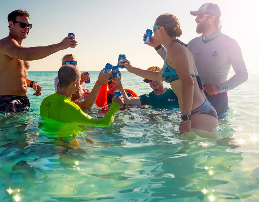 Group of people stood in clear water and celebrating with a canned drink