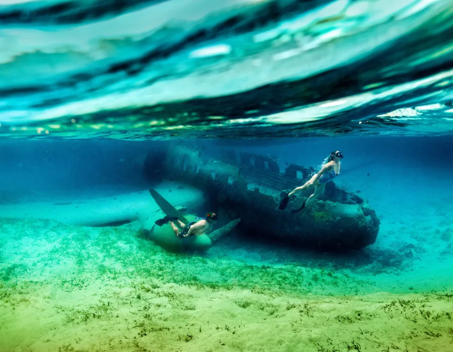 Man and woman snorkelling next to a plane wreck in clear water