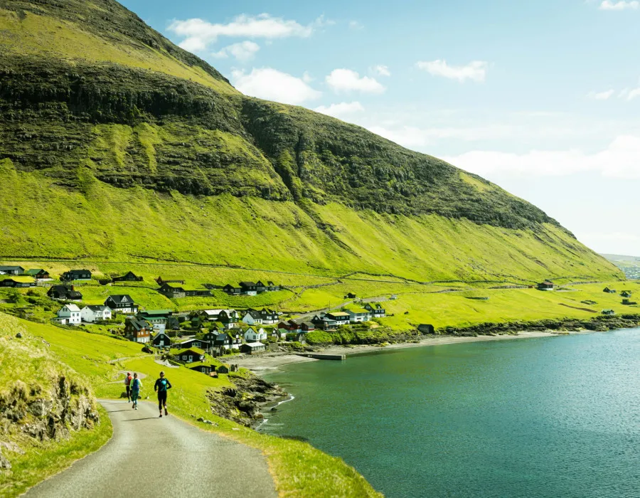 Participants running along sunlit coastal path with houses in the distance