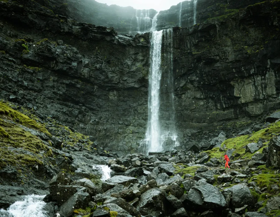Waterfall falling from a high ledge into rocks below with splashes of greenery
