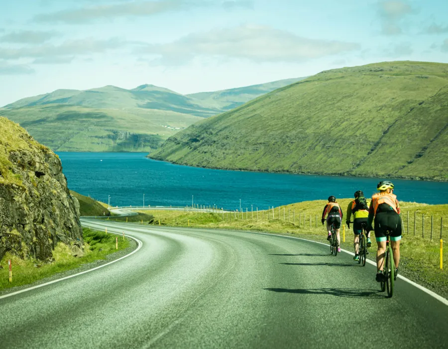Three participants cycling on coast road, past clear water and green mountains
