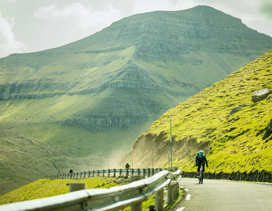 Cyclist riding along road with green mountain in the background