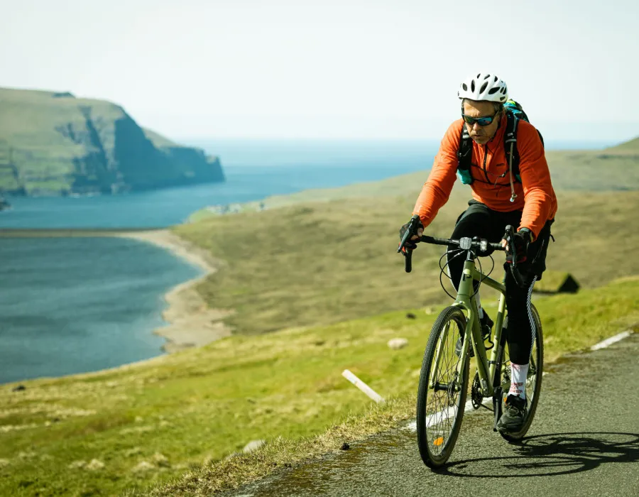 Man cycling along a coastal road with blue water and cliffs behind him