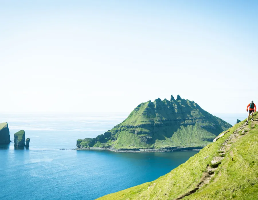 Participants running down steep slope with cliffs and clear water in the background