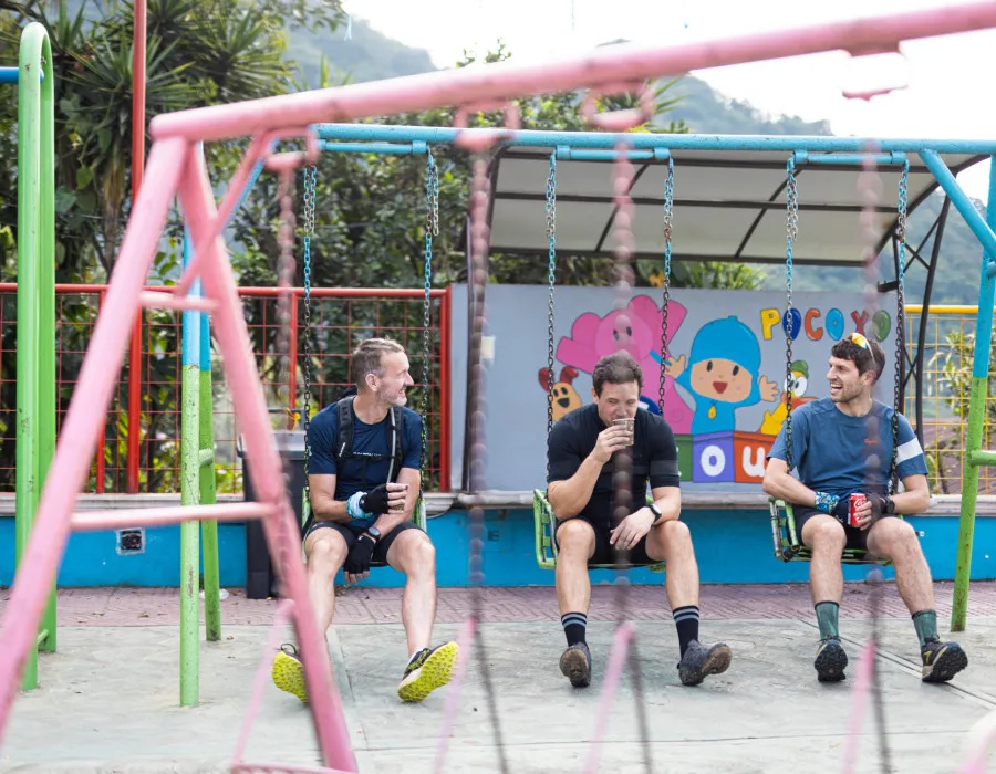 Three men sat on swings in a colourful children's play park