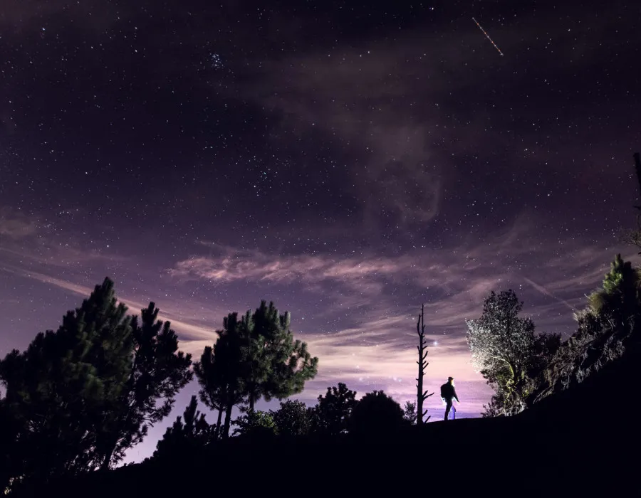 Person hiking with a dark, starry sky above