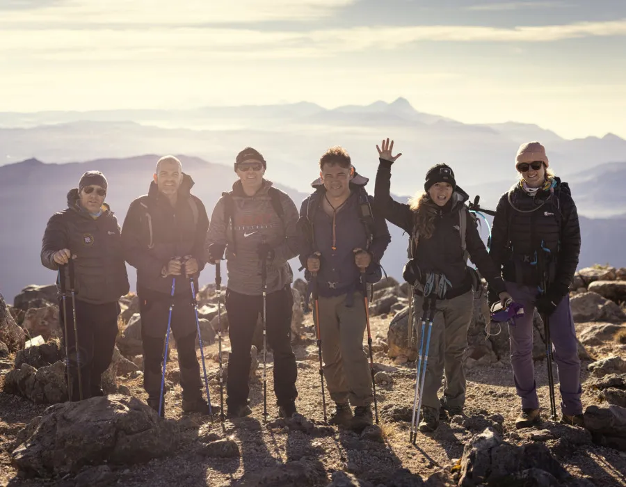 Six people stand on rocky terrain with mountains in the background