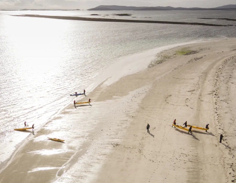 Participants lifting kayaks from water and placing them on sandy beach