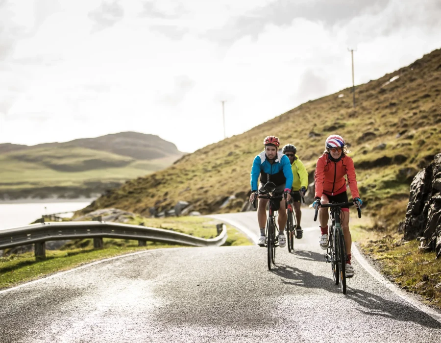 Three cyclists riding along a road with rocky, grassy terrain behind