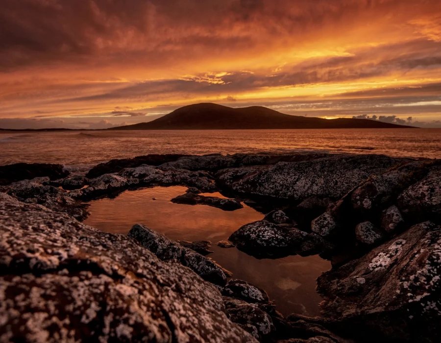 Rocky shoreline and colourful sky with hills in the background