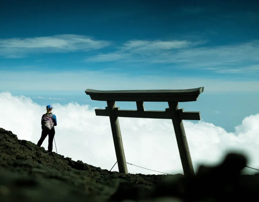 Woman stood on rocky terrain, looking out to bright sky and clouds