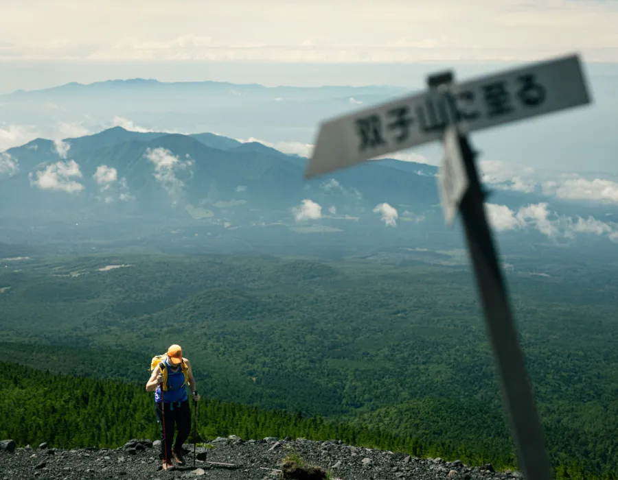 Participant walking with trekking poles and lush, green mountains behind