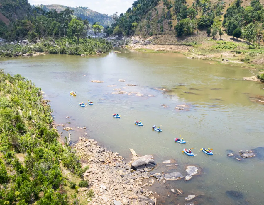 Participants rafting in water surrounded by rocky terrain, sparse trees and mountains