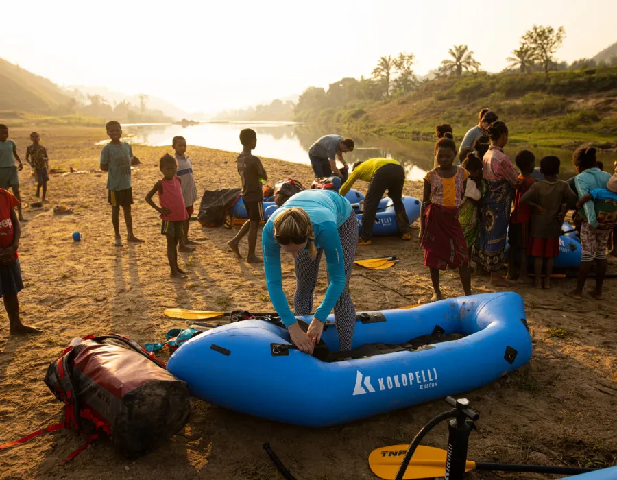 Participants setting up rafts by river and surrounded by local children