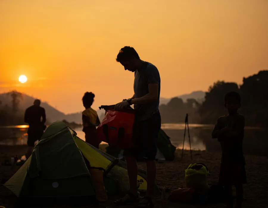 Participants unpacking their tents as a colourful sun sets in the background