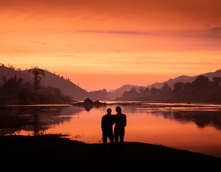 Silhouettes of two participants with their arms around one another with colourful sky above