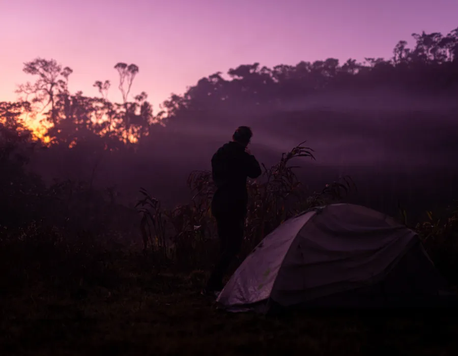 Participant stood by tent, looking out to purple, colourful sky