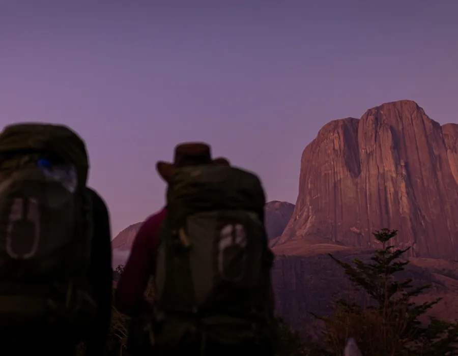 Participants wearing rucksacks and looking up to red mountains