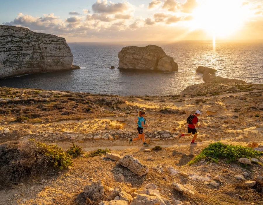 Man and woman running along rocky coastline
