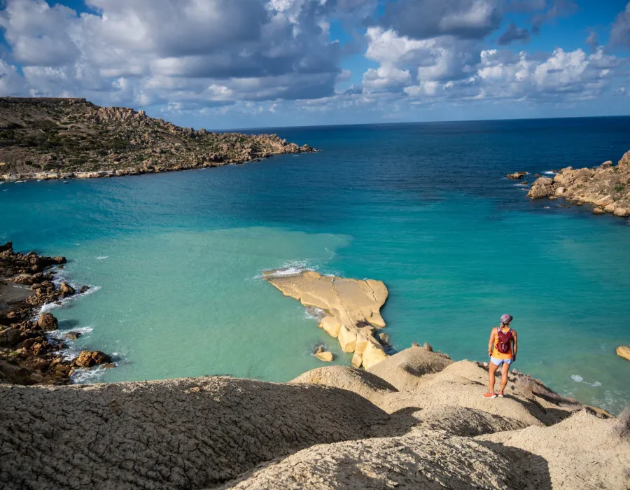 Woman stood on rocks, looking out to clear, still sea