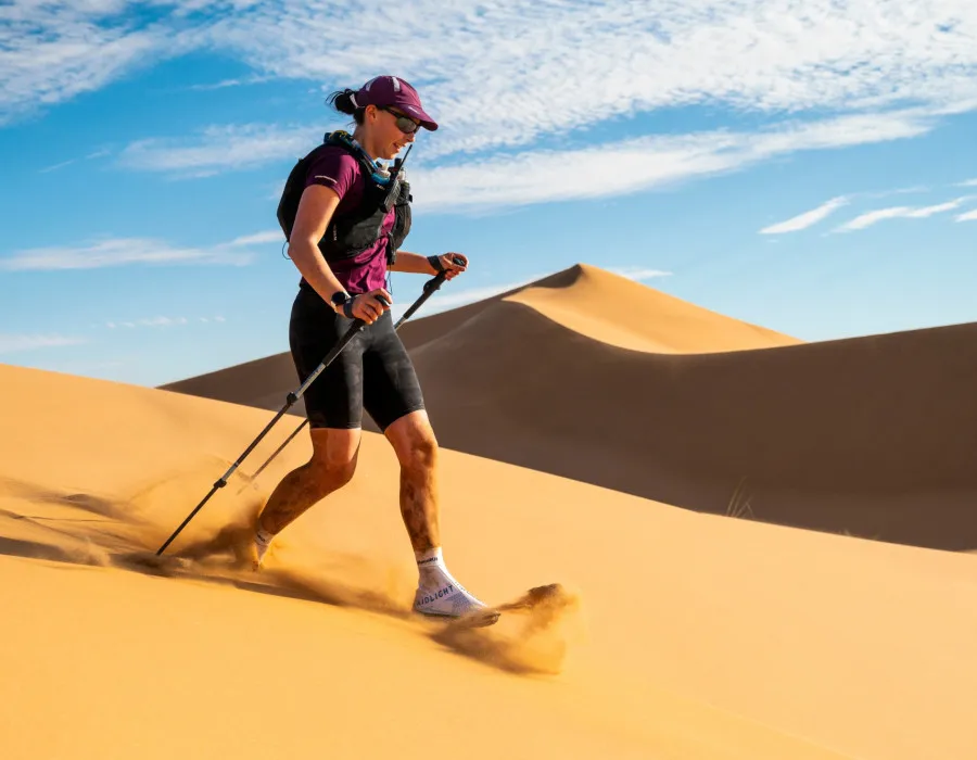 Woman running down sand dune using trekking poles