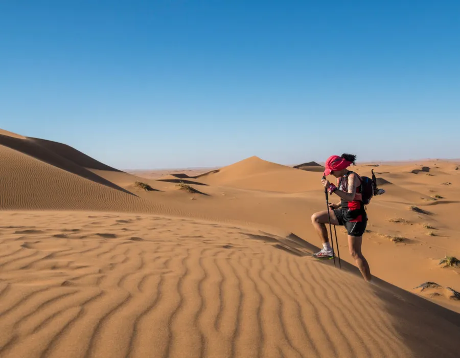 Women walking up sand dune with trekking poles