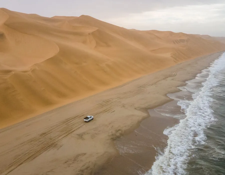 Car travelling along sandy coastline, between sea and sand dunes