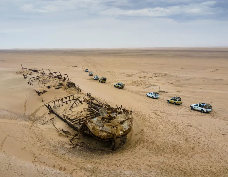 Cars passing past ship wreck in desert