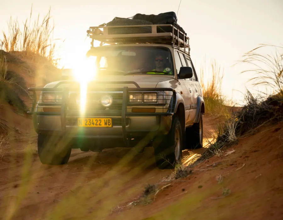 Car driving through sandy and grassy terrain with the sun shining above